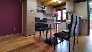 A modern kitchen with wooden cabinets, a dining table with chairs, and a view of the outdoors through a window.