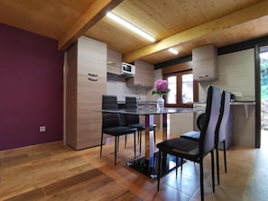 A modern kitchen with wooden cabinets, a dining table with chairs, and a view of the outdoors through a window.
