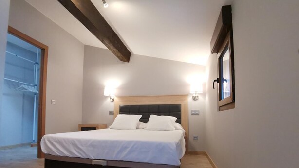 A bedroom with a bed, bedside lamps, a wooden headboard, and a window.