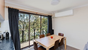 Una habitación con un ventanal grande, una mesa con sillas, una kitchenette pequeña y un ventilador de techo.