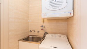 Un bagno compatto con lavatrice e asciugatrice integrate, lavandino in acciaio inossidabile e porta asciugamani.