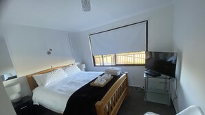Ett hotellrum med en säng, en tv, en stol och ett fönster med utsikt över omgivningen.