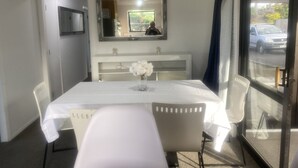 Ett hotellrum med ett vitt bord, stolar, en vas med blommor, en spegel och ett fönster med utsikt över en gata och parkerade bilar.