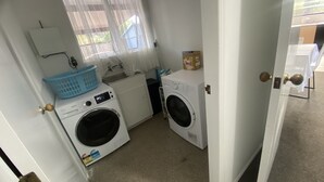 Ett litet och praktiskt tvättrum med tvättmaskin, torktumlare och ett fönster med tunna, genomskinliga gardiner.