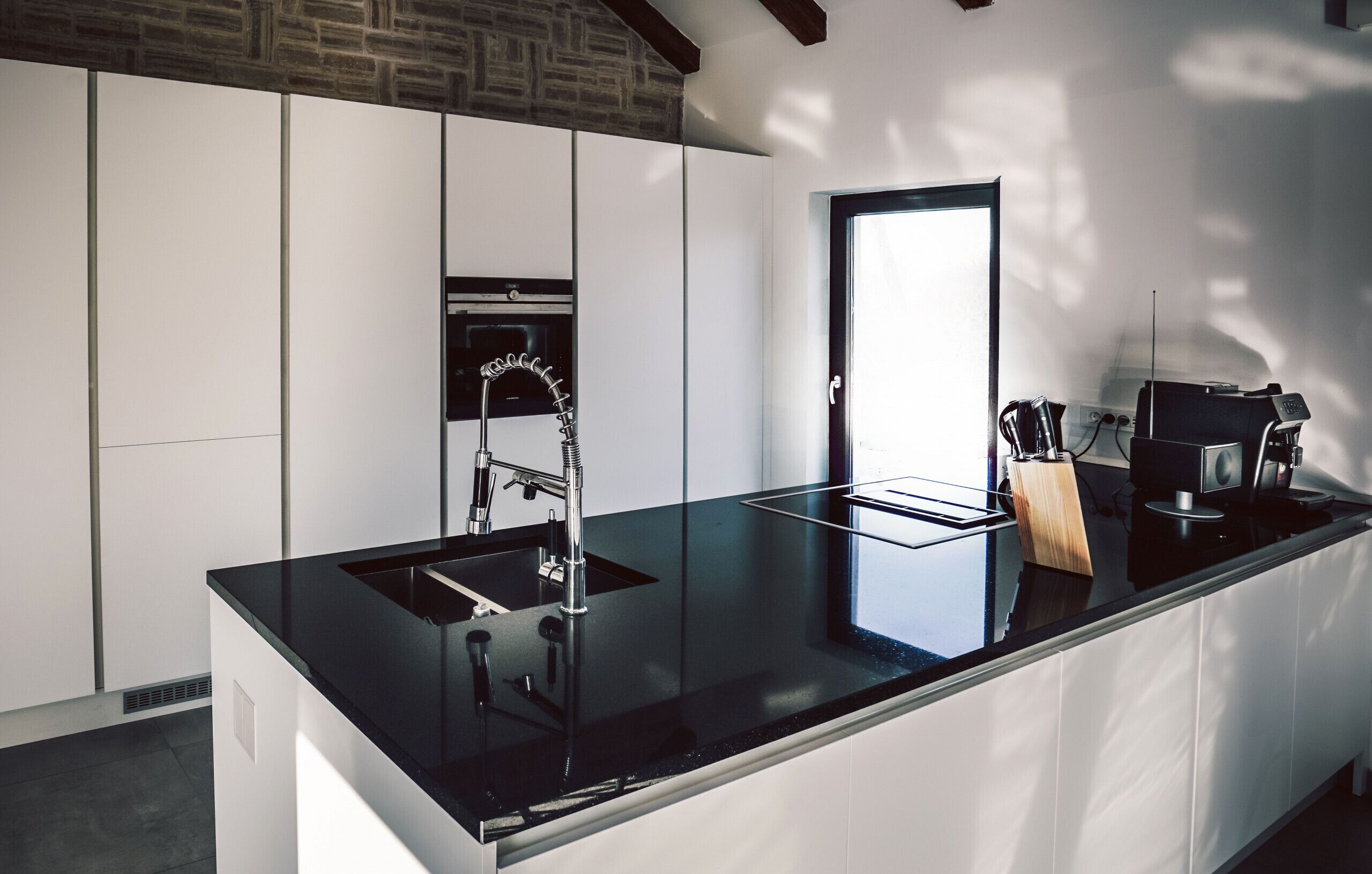 Uma cozinha moderna com bancada preta, torneira de aço inoxidável e forno embutido.