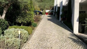 Un chemin pavé de pierres menant à un bâtiment à la façade blanche, avec un ciel bleu en arrière-plan.