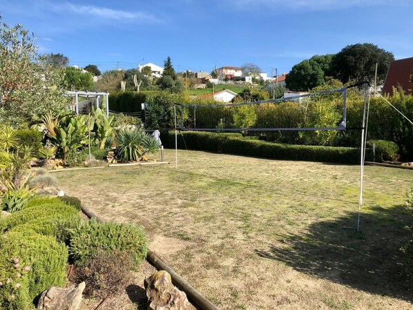Quintal com uma rede de voleibol, diversas plantas e um caminho de pedra.