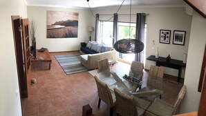 Un salon comprenant un canapé, une table à manger et des chaises, un tableau accroché au mur et une fenêtre avec des rideaux.