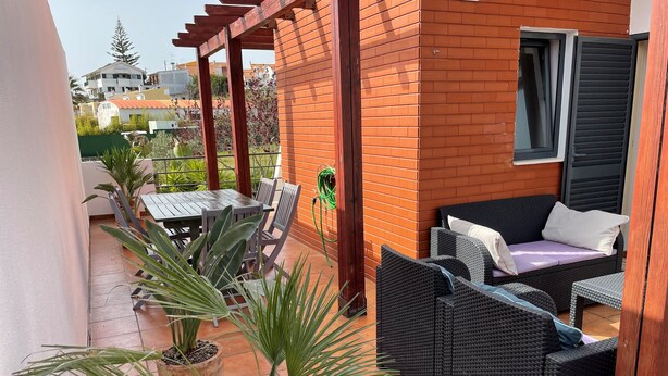 Une terrasse couverte avec une table et des chaises, un canapé en osier et des plantes en pot.