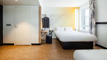 A modern hotel room with a wooden floor, a bed, a desk with a chair, a wardrobe, and a window with curtains.