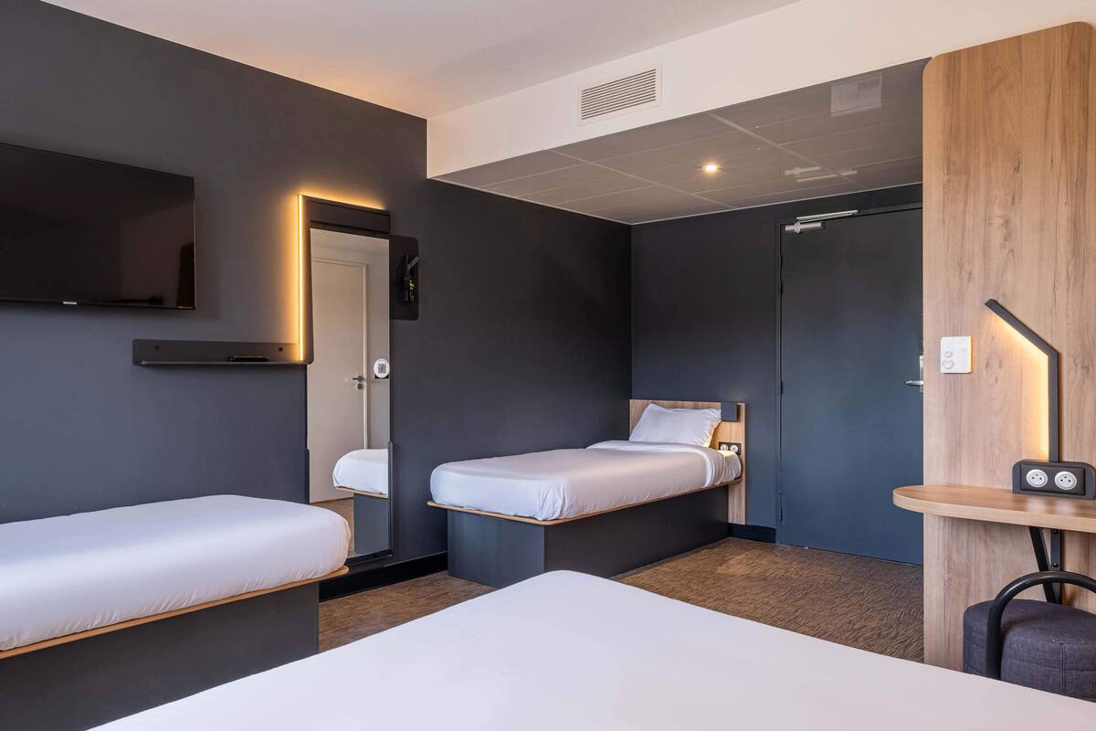 Ein modernes Hotelzimmer mit zwei Einzelbetten, einem wandmontierten Flachbildfernseher, einem Nachttisch mit Lampe und einer Wand mit Holzvertäfelung.