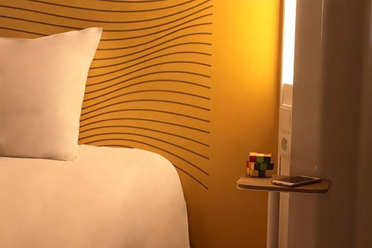 Habitación de hotel con una cama, una mesita de noche con un teléfono y un objeto pequeño, y una pared con un diseño único.