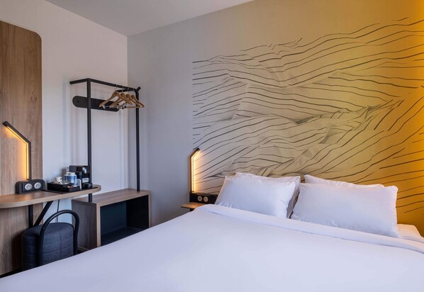 Ein Hotelzimmer mit einem Bett, einem Schreibtisch mit Stuhl, einem Kleiderständer und einer Wand mit strukturierter Gestaltung.