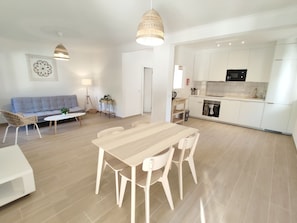 A modern kitchen with white cabinets, a microwave, and a stove. There is a dining area with a wooden table and chairs.