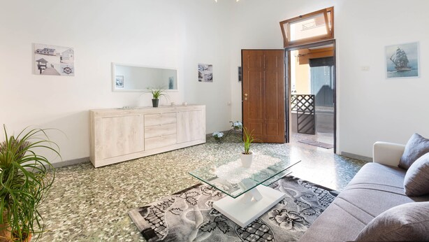 Uma sala de estar moderna com uma mesa de centro de vidro, um sofá, um armário de madeira e uma porta que dá para uma área externa.