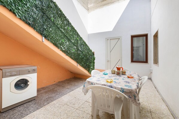 Een kleine wasruimte met een wasmachine, een tafel met stoelen en een groene wand.