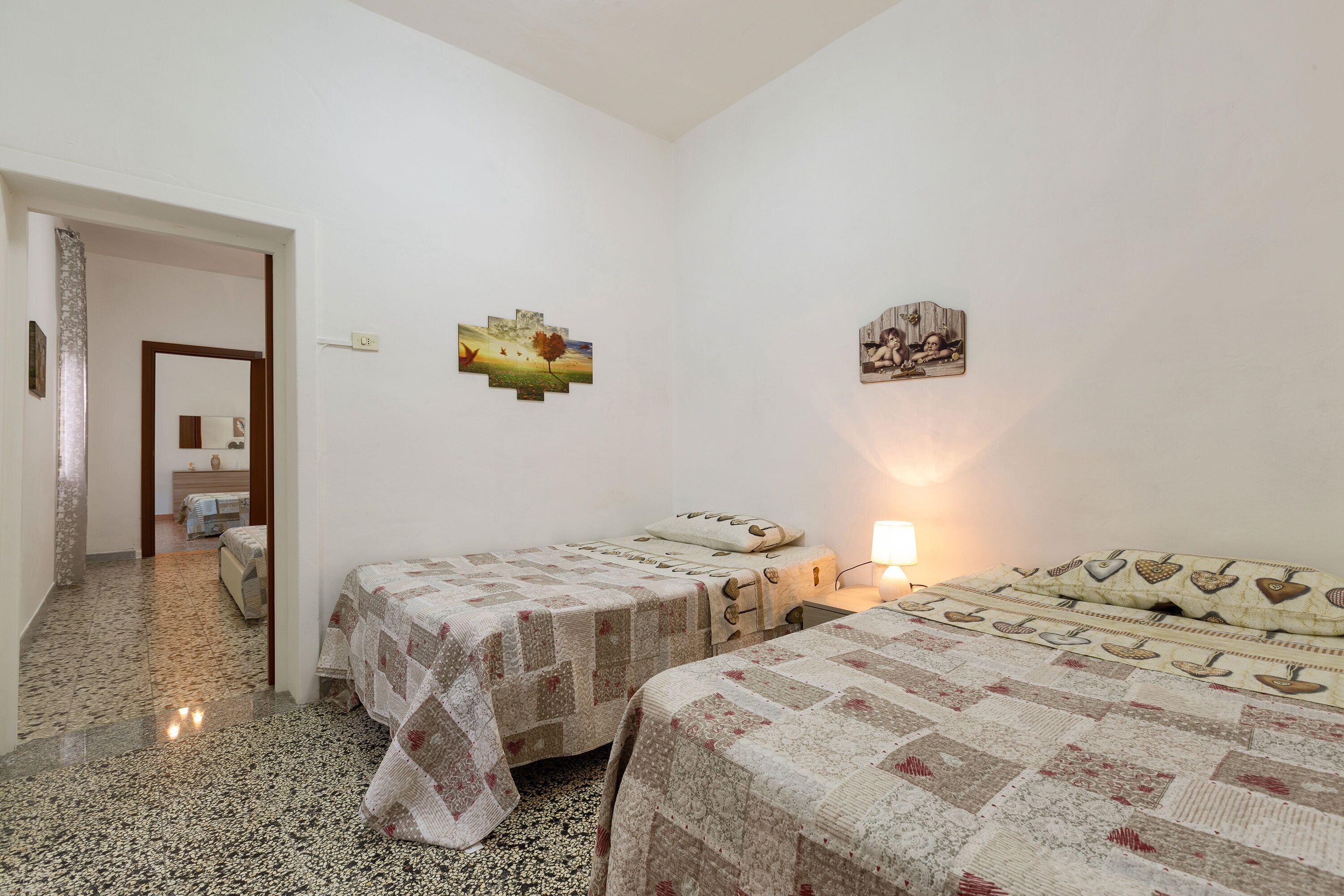 A room with two beds, a small table, and a wall-mounted lamp.