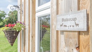 Un edificio de madera con un letrero que dice "Buttercup" y una maceta colgante de flores.