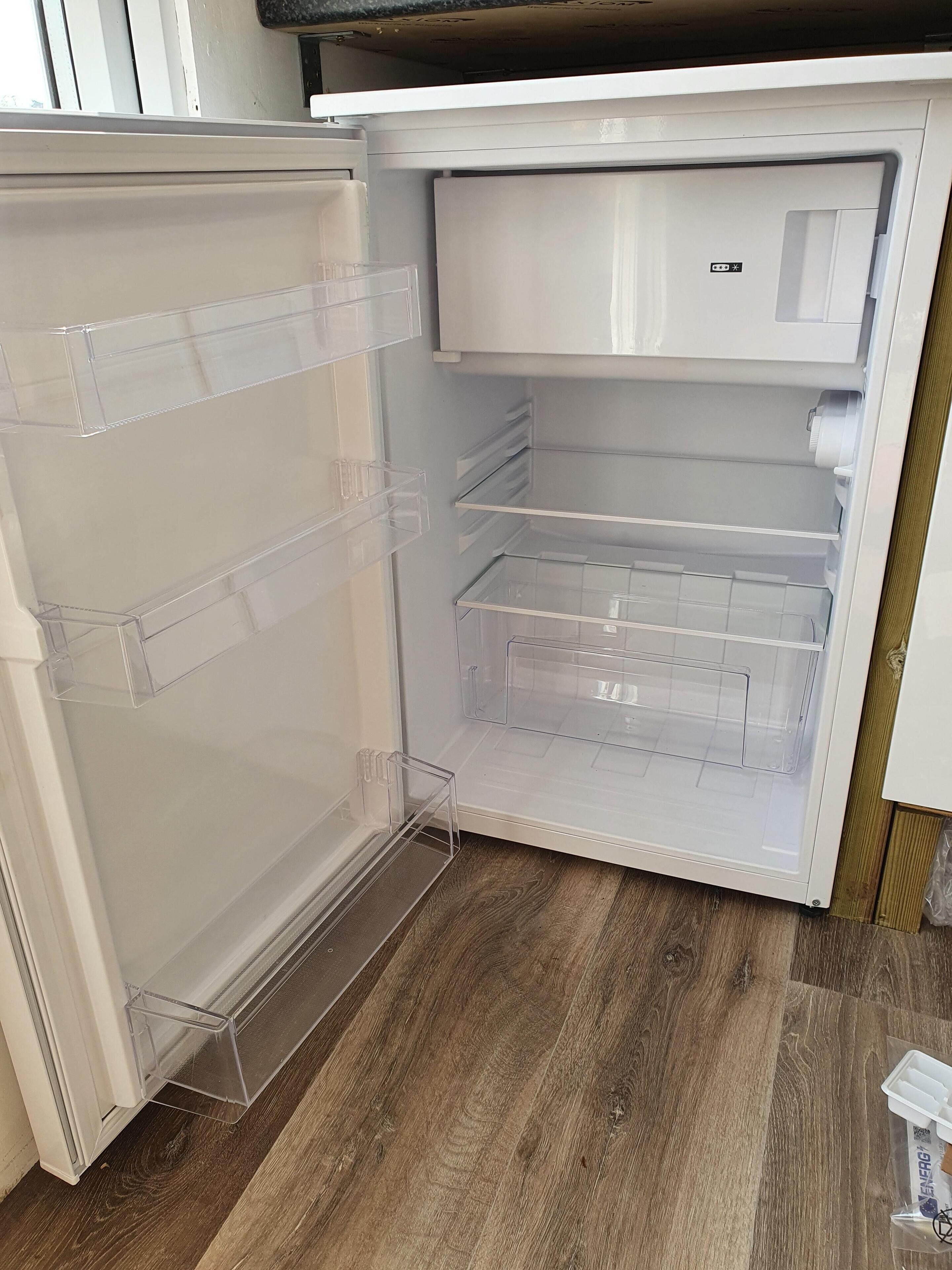 An open refrigerator with clear plastic shelves and a wooden floor.