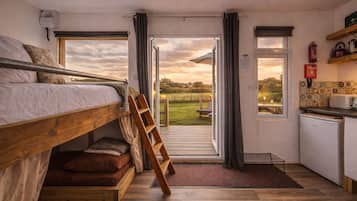 A compact room with a bunk bed, a small kitchenette, and a view of a grassy field.