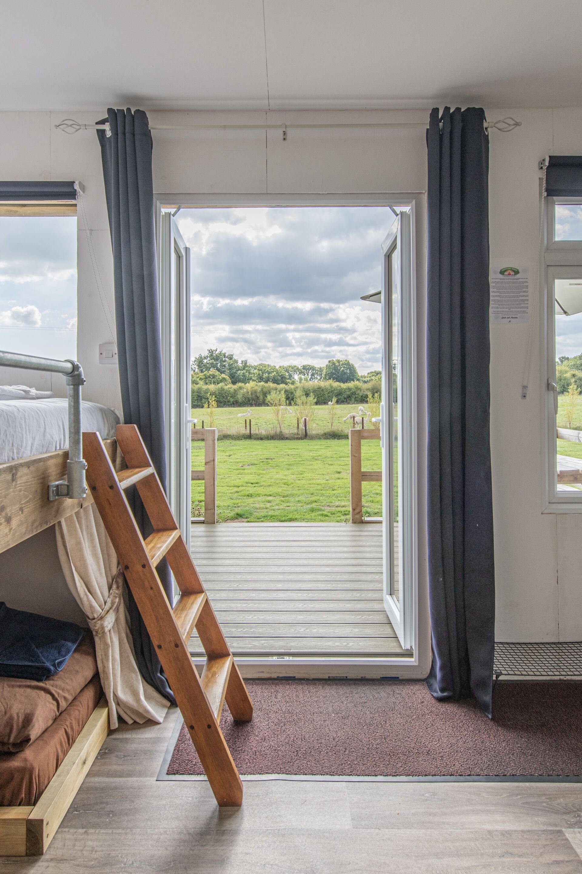 A room with a wooden ladder, a bunk bed, and a large sliding glass door leading to a grassy outdoor area.