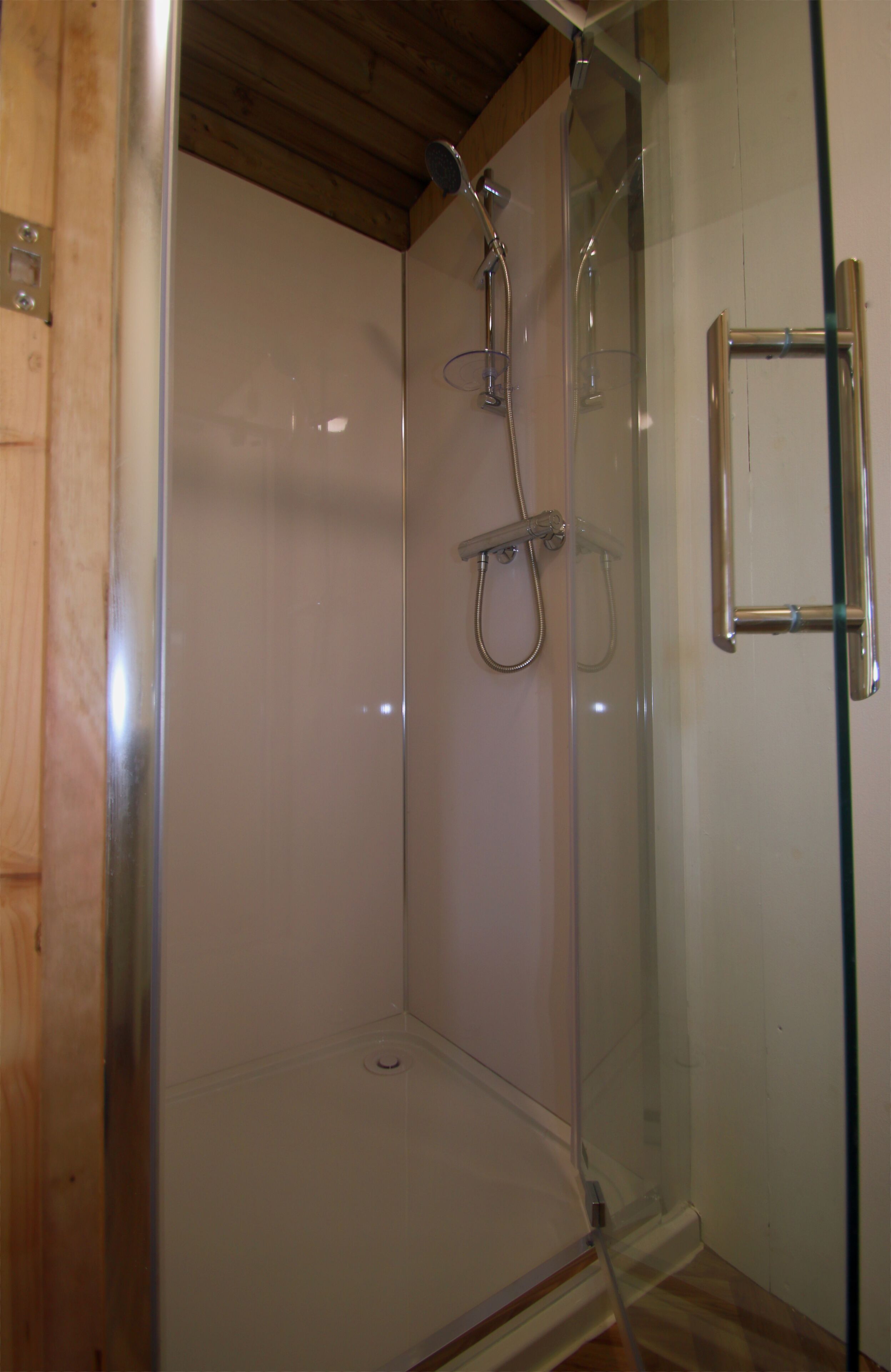 A glass-enclosed shower with a wooden ceiling and a metal towel rack.
