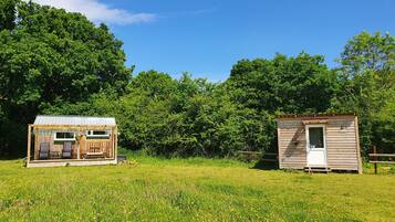 Dos cabañas de madera en un campo cubierto de hierba, con árboles al fondo.