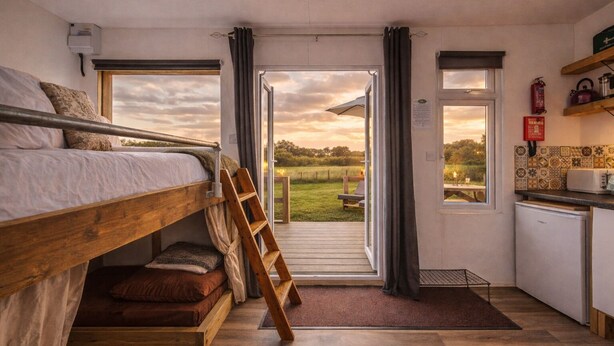 Una habitación pequeña con literas, una kitchenette compacta y vistas a un campo verde.