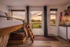 A compact room with a bunk bed, a small kitchenette, and a view of a grassy field.