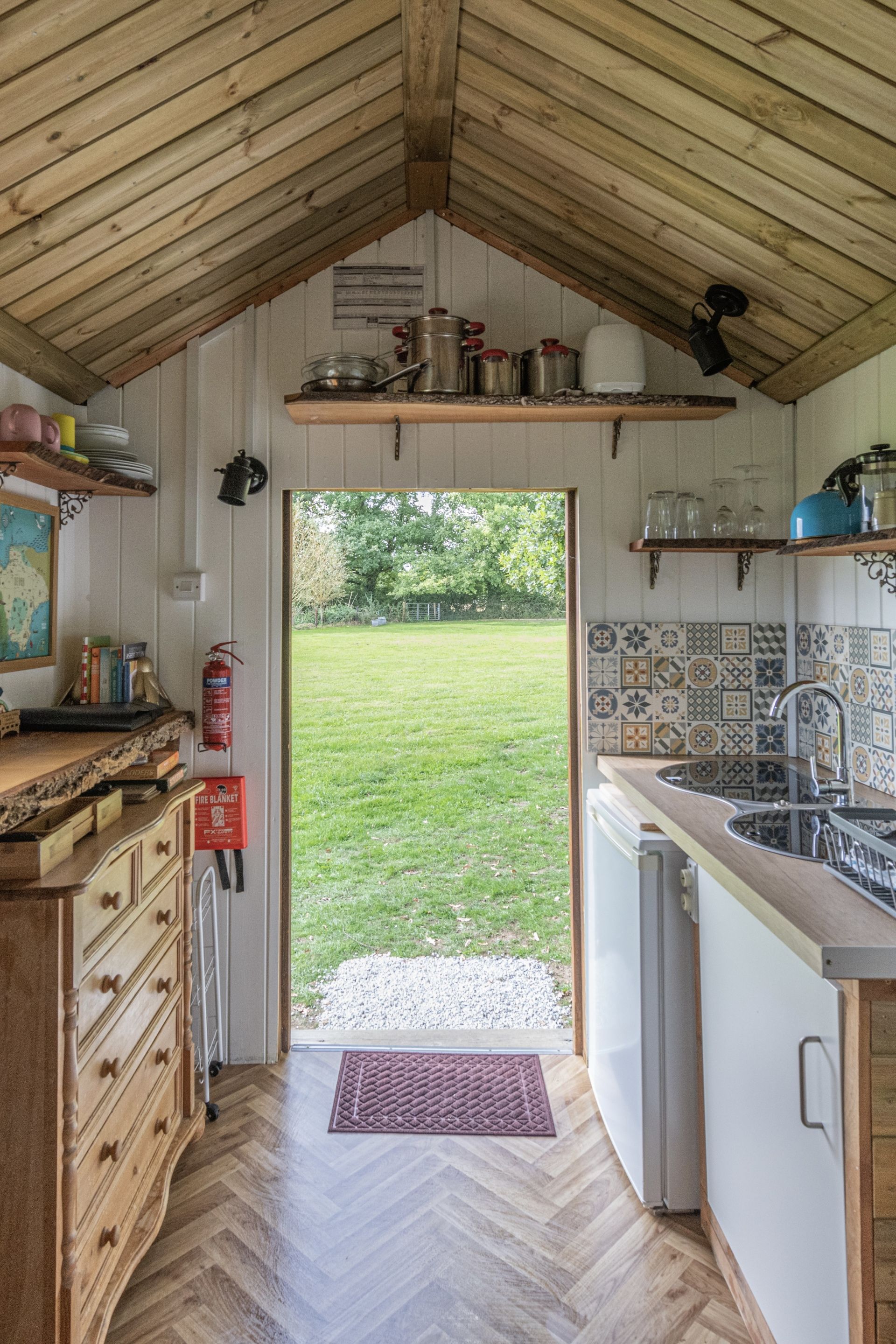 Una cucina con soffitto in legno, pavimento a spina di pesce, un lavandino e vista su un prato.