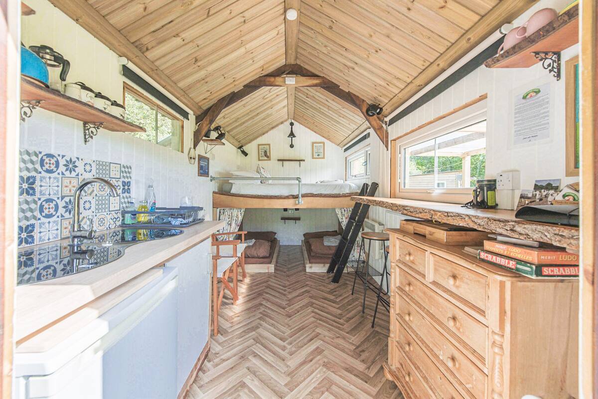 A compact kitchen with wooden flooring, a herringbone pattern backsplash, and a small dining area with a bench.