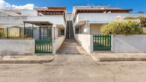 A narrow alleyway with buildings on either side, a green gate, and a staircase leading to a higher level. - 1868 A Casa di Luciano (Uggiano la Chiesa)