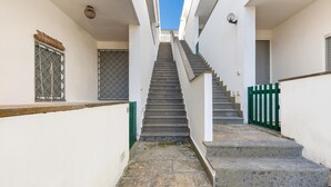 A narrow, stone-floored stairway leading to a door, flanked by white walls and a green gate. - 1868 A Casa di Luciano (Uggiano la Chiesa)