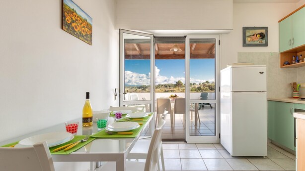 A dining area with a table set for two, a refrigerator, and a view through glass doors to an outdoor patio. - 1868 A Casa di Luciano (Uggiano la Chiesa)