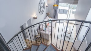 Eine Treppe führt zu einem Wohnbereich im modernen Stil, inklusive einer Uhr, Pendelleuchten und einem Sofa mit dekorativen Kissen.