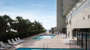 A swimming pool with lounge chairs, palm trees, and a building with large windows. - Beautiful Ocean view corner unit (Myrtle Beach)