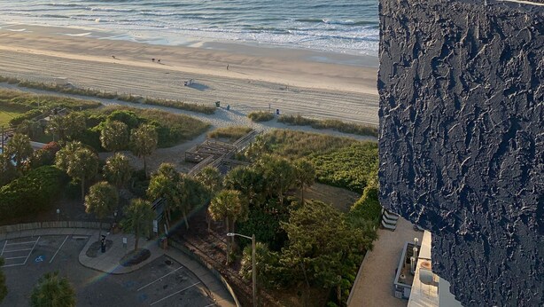 A coastal view from a building with a rocky facade overlooking a beach and ocean. - Beautiful Ocean view corner unit (Myrtle Beach)