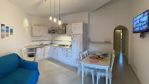 Cocina compacta con comedor, sofá y televisor montado en la pared.