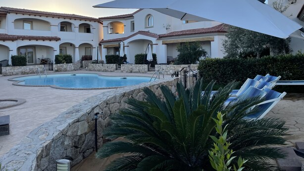 Zona de piscina con muro de piedra, sillones de descanso y una sombrilla grande.
