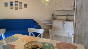Una sala de estar acogedora con un sofá azul, una mesa de comedor con mantel decorativo y una cocina con fregadero y armarios.
