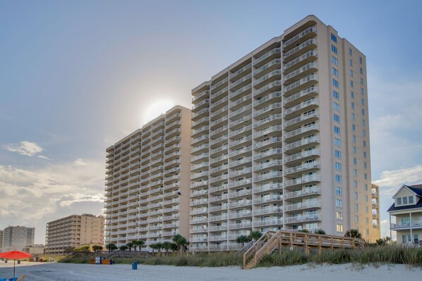 A high-rise hotel with multiple balconies, located near a beach.