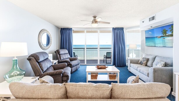 A living room with a sofa, armchairs, a coffee table, a TV, and a view of the ocean.