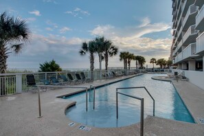 A swimming pool with lounge chairs and palm trees, surrounded by a white fence. - Luxury oceanfront condo - Indoor/Outdoor Pools + Free Attraction Tickets! (North Myrtle Beach)