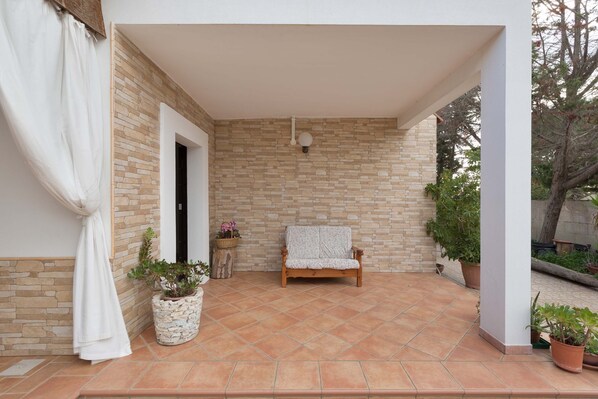 A covered patio with a stone wall, a wooden bench, and potted plants.