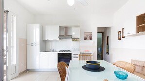 A modern kitchen with white cabinets, a dining table with chairs, and a blue bowl on the table. - 1890 Bilo Conchiglia Blu (Porto Cesareo)