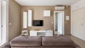 A modern living room with a flat-screen TV, a white console table, and a large window. - 1866 Stella Bianca Luxury Suite (Lecce)