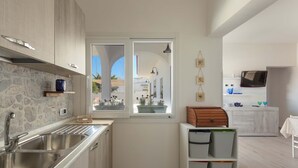 A modern kitchen with a stone backsplash, stainless steel sink, and a view of the outside. - 1939 Villetta Camilla (Lecce)