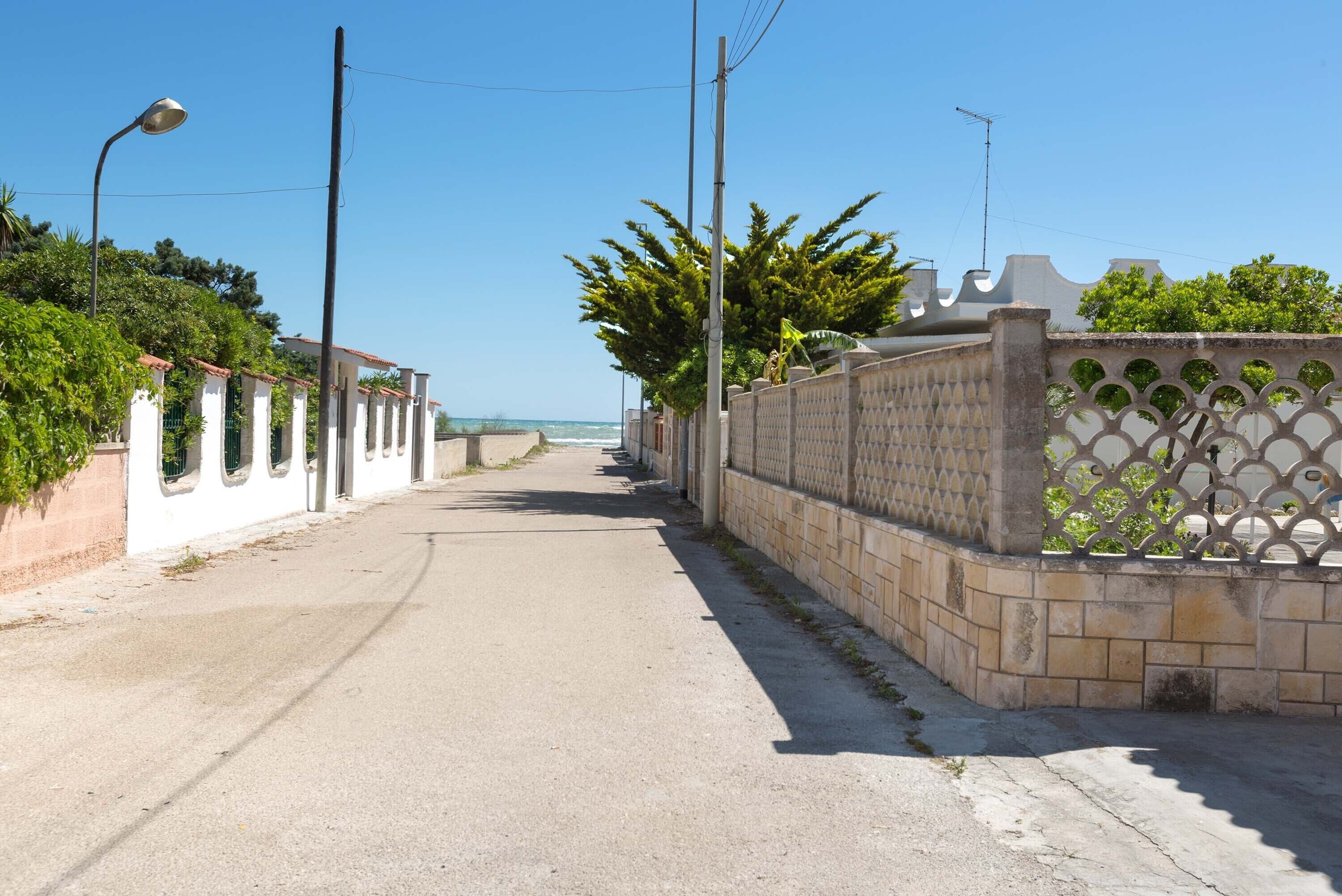 A narrow street flanked by white buildings with arched windows and a decorative fence.
