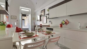 A modern kitchen with white cabinetry, a dining table with chairs, and a large window providing natural light. - 1991 Suite Verdi (Lecce)