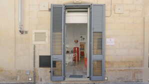 A hotel entrance with a double door, a visible interior including a red sofa and a refrigerator, and a sign with text. - 1991 Suite Verdi (Lecce)